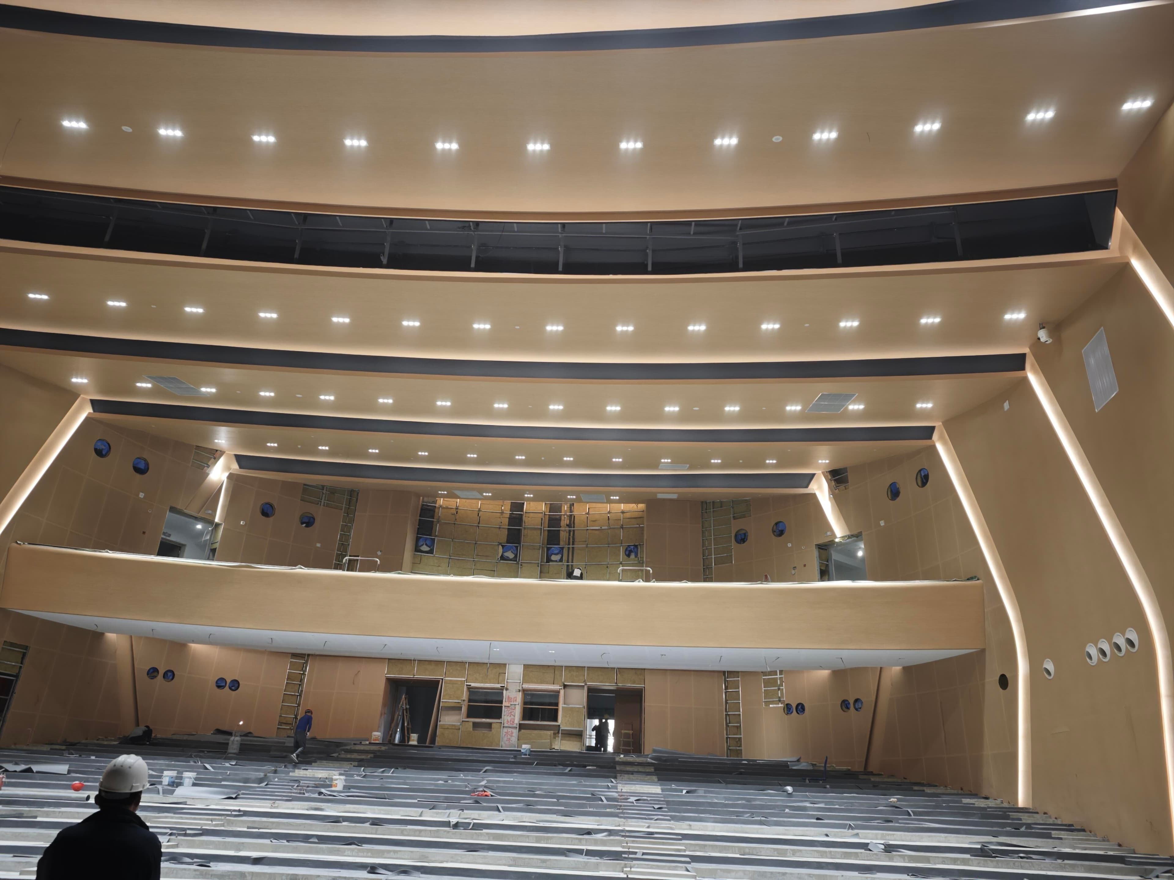 Auditorium construction phase showing balcony edge, ceiling lighting slots, and seating base