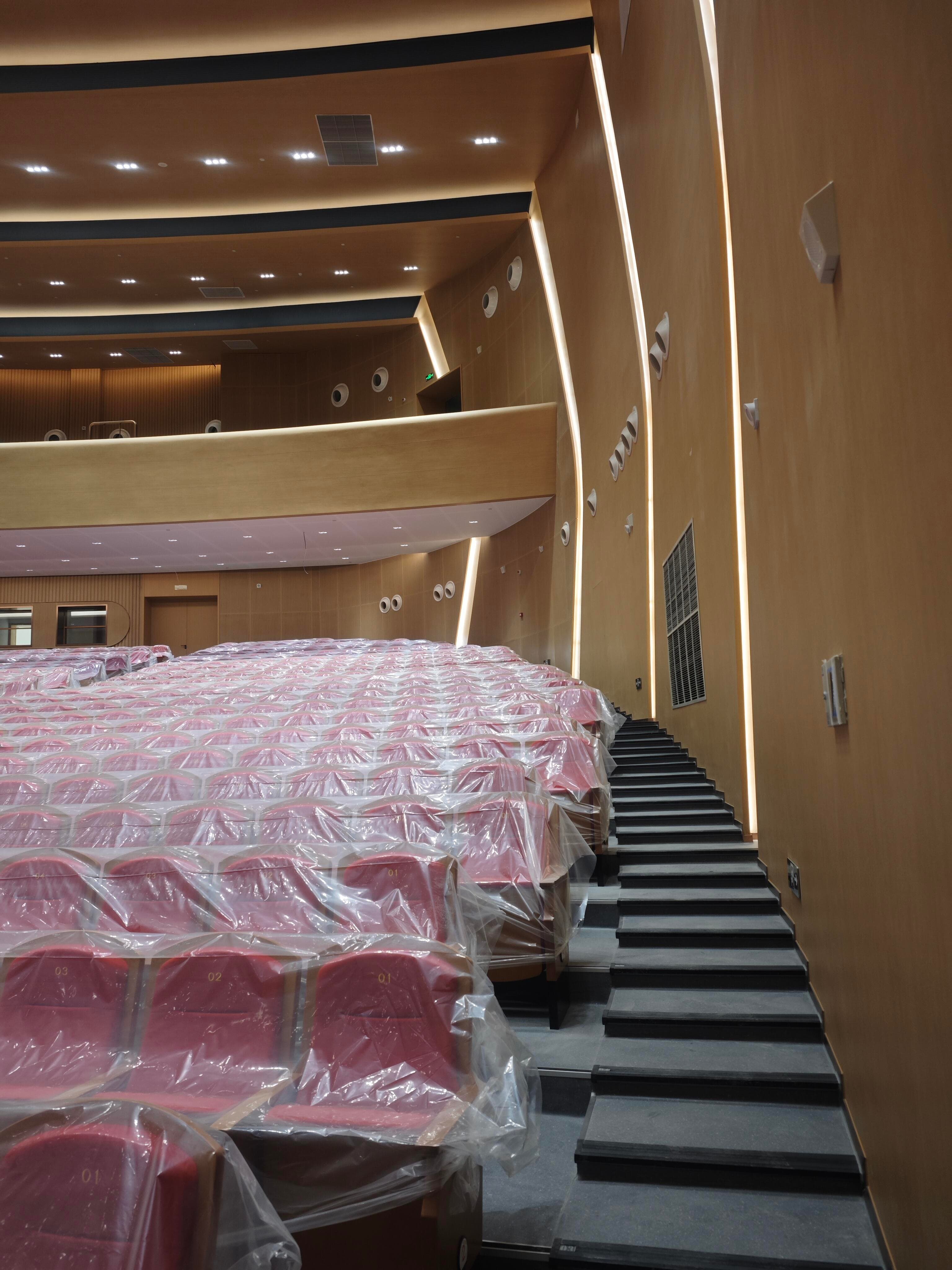 Auditorium side aisle and covered red seats beside acoustic wall panels