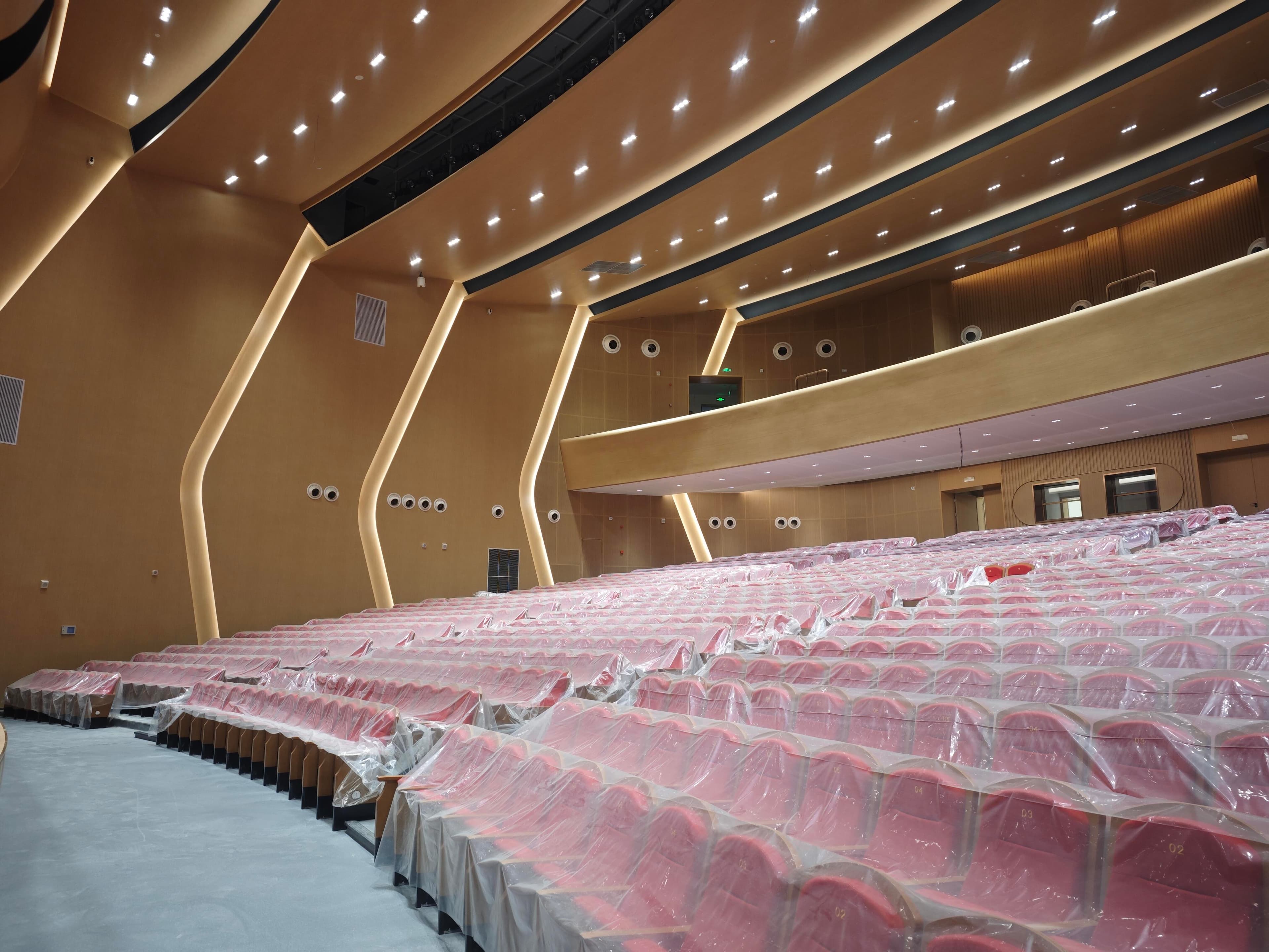 Auditorium lower seating bowl beneath the balcony with red fabric seats and folded wall lighting