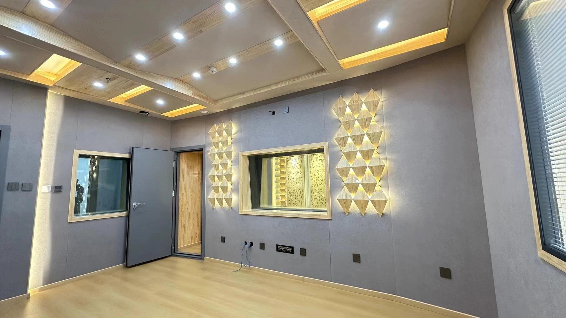 Recording room wall with acoustic observation windows and triangular backlit wooden diffusers