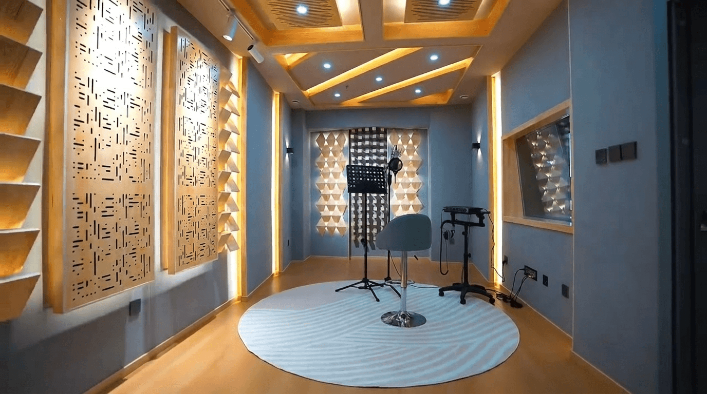 Finished live room with condenser microphone, music stand, round rug, high stool, and acoustic diffuser walls