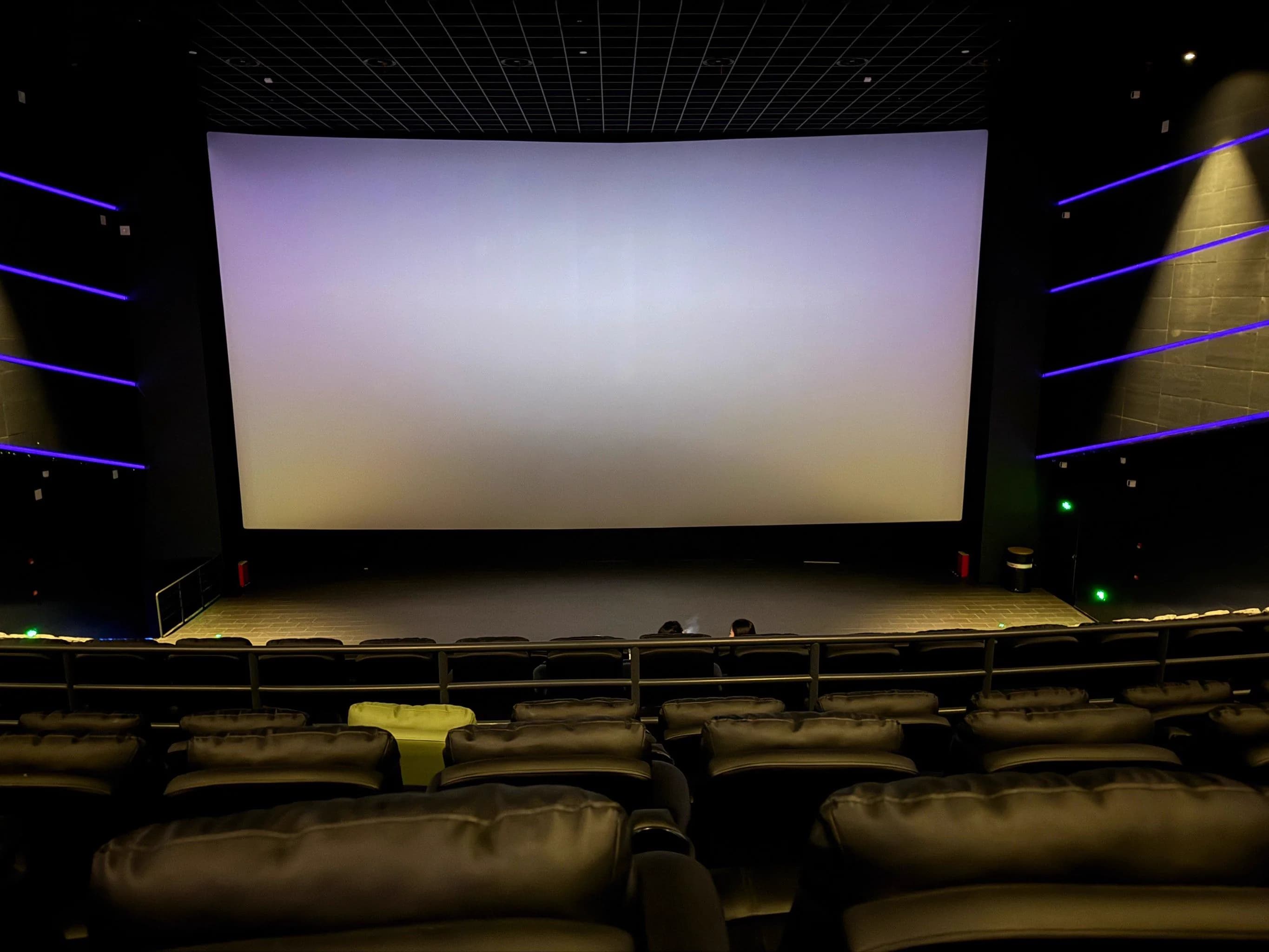 Rear-side auditorium view showing the giant screen, raked seating, and dark field lighting